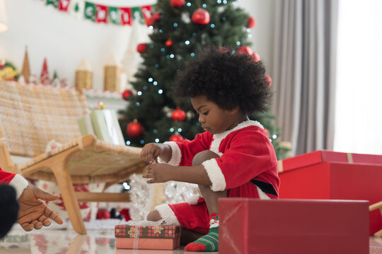 African American father celebrates Christmas and give Christmas gift box to little son in festive living room. Happy cute African American little boy with Chirstmas gift box