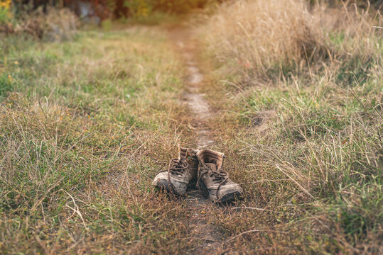 Pair of old worn shabby shoes with dusty cracked leather and untied laces standing in dry grass