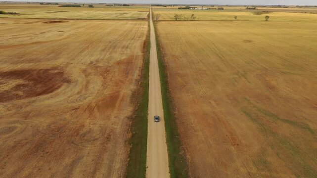 Car driving down a rural dirt road through expansive farmland