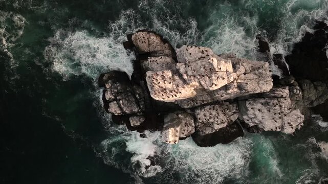 Top down aerial view of waves churning around a white sea rock