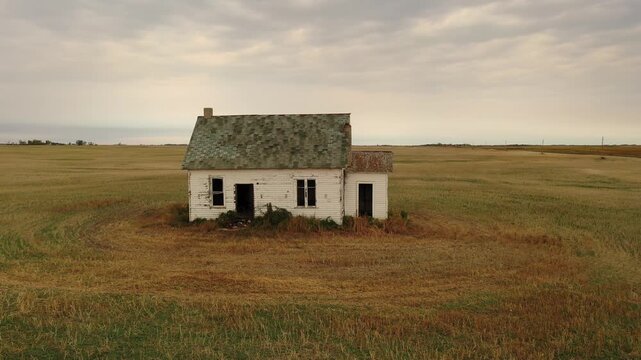 Abandoned farmhouse in rural field under cloudy sky