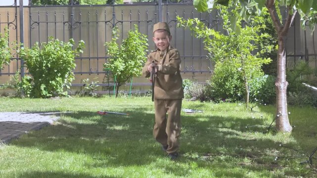 A child in military costume falls onto the lawn as part of an imaginative war game outdoors. 