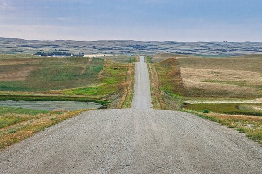 Rural Gravel Road Crossing the Open Southern Saskatchewan Prairie with the View of Dirt Hills on the Horizon