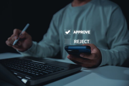 Person uses a smartphone and stylus beside a laptop to approve a digital decision