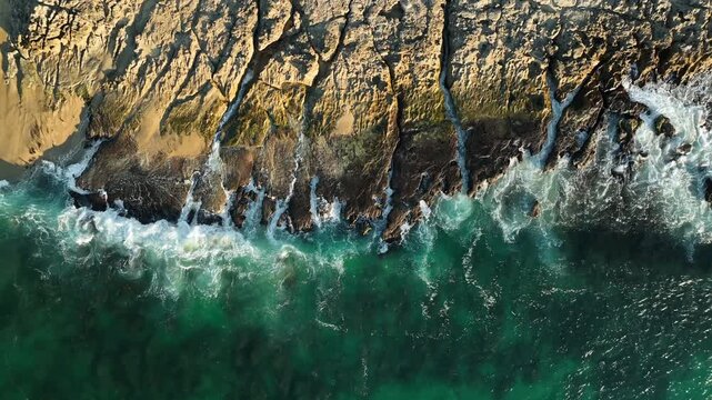 Aerial top down view of waves crashing against a flat rocky shelf