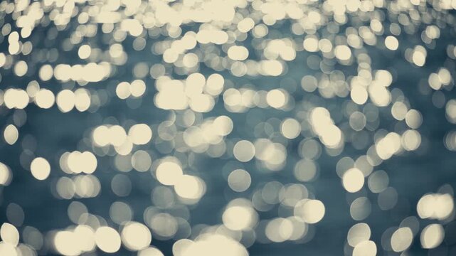 Abstract 4K video of rippling water texture with bokeh sunlight sparkling with lights reflected, blur in foreground and background.