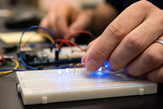 Close-up of an engineer placing a resistor onto a breadboard circuit with lit blue LED lights during a science experiment.