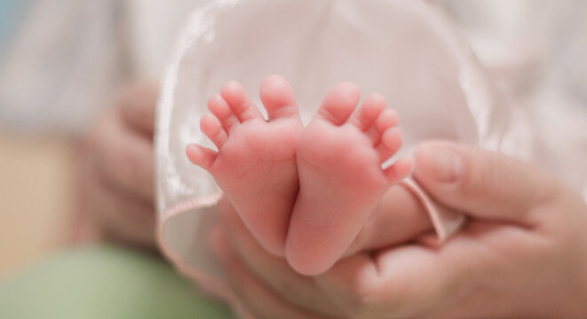 Infant care, tenderness, family bonding, and early childhood. Close up of newborn baby feet gently supported by an adult hand, with soft natural light and pastel colors.