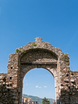 Low-angle view of the historic Porta Catania stone archway gate in Taormina, Sicily, Italy.