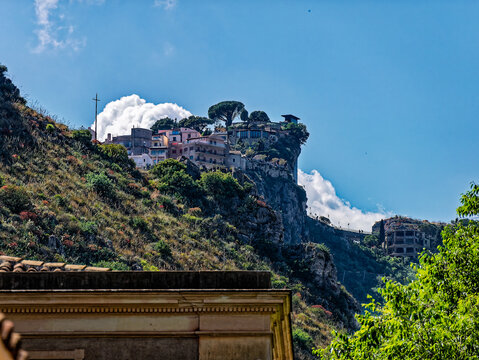 Breathtaking Sicilian landscape featuring Taormina's iconic hilltop village, with terracotta homes and stone pines clinging to steep, vegetation-covered cliffs.