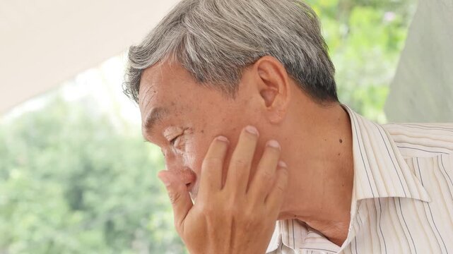 senior east asian man in his 60s scratching his itchy cheek and face