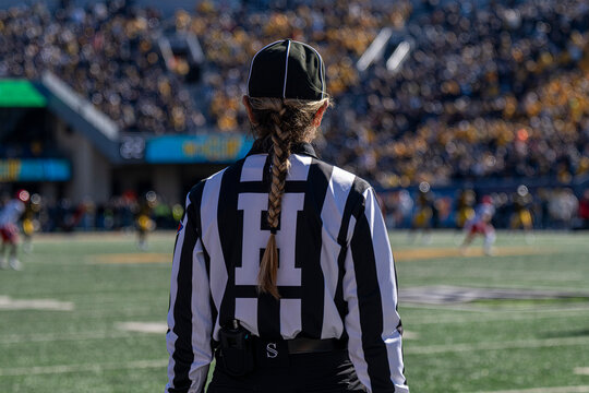 Back View Of Football Referee Official In Striped Uniform Watching Game In Sunny Stadium Crowd