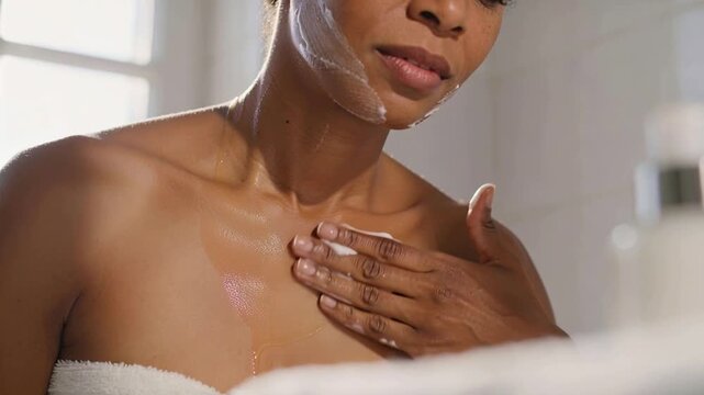 Applying woman in white towel spreading cream jawline to chest by window, prompted by shiny oil