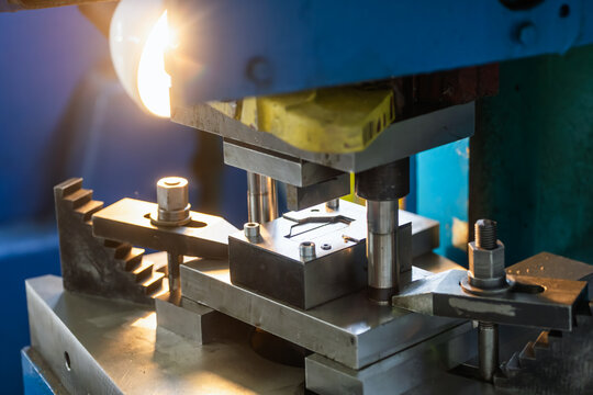 Close-up of punch press operator positioning metal blank inside stamping die during production of metal components in manufacturing workshop