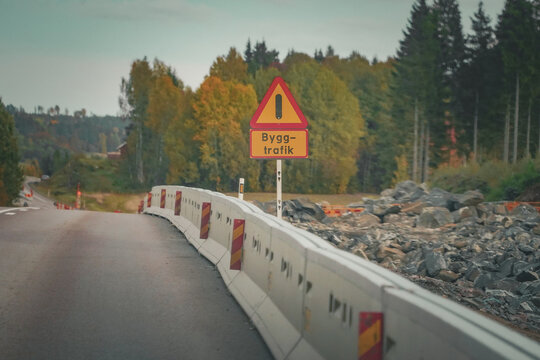 View of a road construction sign reading Bygg-trafik with concrete barriers along an asphalt road surrounded by autumn trees in Karlstad, Varmland County, Sweden.