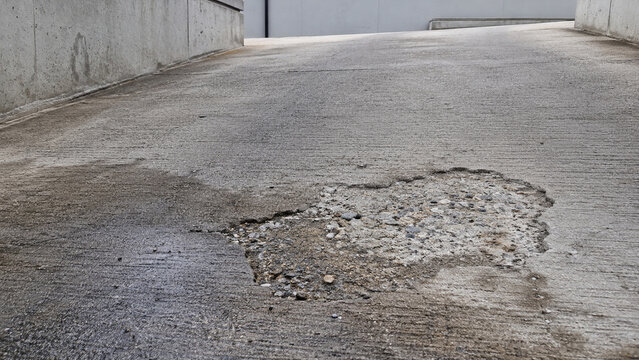 Shallow pothole exposing aggregate on wet concrete access ramp surface