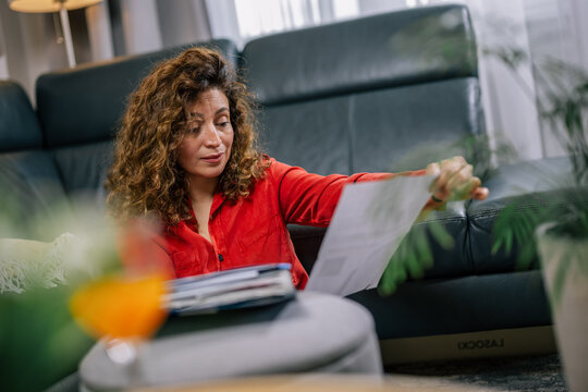 Concerned woman reading official letter while sitting on living room floor