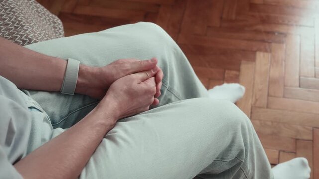 Finger tapping and nervous hand fidgeting on lap as anxious man sits on bed, rubbing thumb repeatedly while bouncing leg during stressful moment.