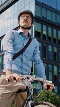 Man pauses on bicycle against modern glass office building