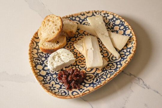 View of a selection of artisanal cheeses, crusty bread slices, and a dark savory spread served on a decorative patterned plate in La Paz, Baja California Sur, Mexico.
