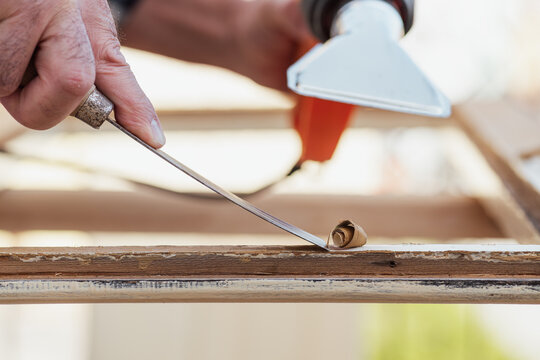 Carpenter using heat gun and wood scraper removes paint from old wooden window. Construction industry, carpentry. Restoration. 