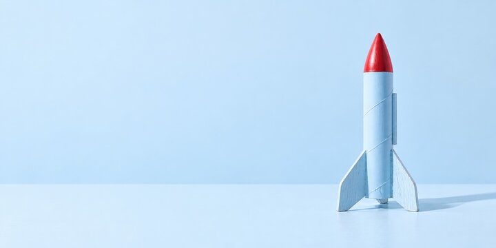 Model rocket with a red tip on a pale blue surface, featuring a hand-painted satin finish and ample copy space for World Space Week and STEM education