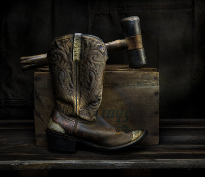 Old cowboy boot and old rubber mallet, with old wooden box in still life.