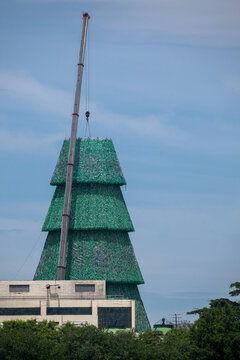 View of a large green tiered structure resembling a Christmas tree being assembled by a tall crane against a clear blue sky in Rio de Janeiro, Rio de Janeiro, Brazil.