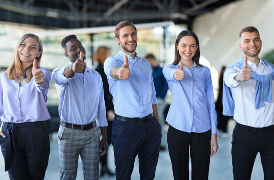 Happy businesspeople standing in office showing thumb up.