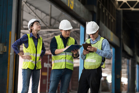 Workers, warehouse storage and logistics. Diverse group of warehouse workers wearing safety hard hats discussing inventory management and operations logistics planning in industrial storage warehouse