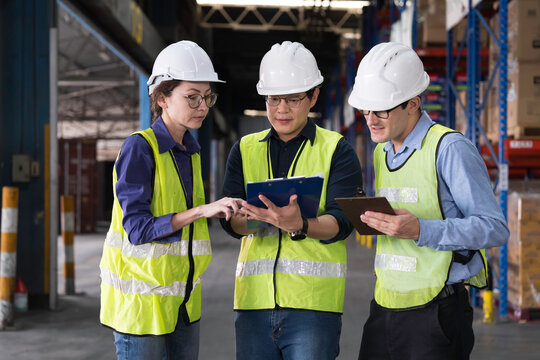 Workers, warehouse storage and logistics. Diverse group of warehouse workers wearing safety hard hats discussing inventory management and operations logistics planning in industrial storage warehouse