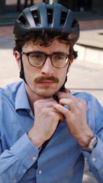 Man fastens helmet strap near bicycle on sunny office plaza