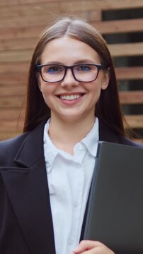 Young woman in glasses posing outdoors in a city park, looking to the side and then smiling at the camera. Slow motion