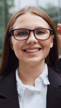 Close-Up of young beautiful woman smiling and looking at camera in front of modern glass building. Slow motion