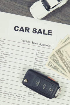 White toy car, car key, dollar banknotes and vehicle sales agreement. Sales or purchases new or used vehicle