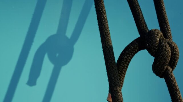 Close-up of a knotted dark braided rope and its shadow on a turquoise boat hull in warm sunlight, French Riviera, France.