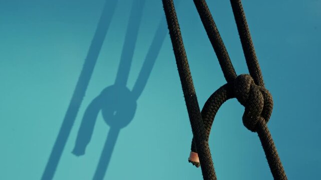 Knotted dark braided ropes casting a sharp shadow on a turquoise boat hull in low evening sun, French Riviera, France.