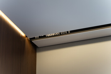 Curtain track with hooks under ceiling and warm LED strip above wooden slat wall panel © Sergey