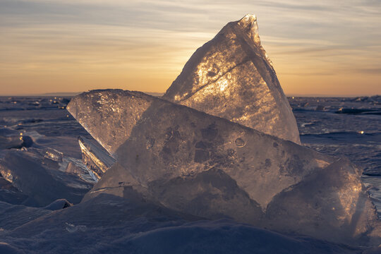 View of large, jagged ice shards on the frozen surface of Lake Baikal, illuminated by the warm glow of a golden sunset in Russia.