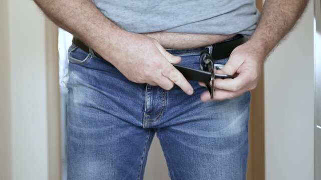 Overweight Man Struggling to Fasten Belt on Jeans Closeup. Man with Big Belly Trying to Buckle Leather Belt.