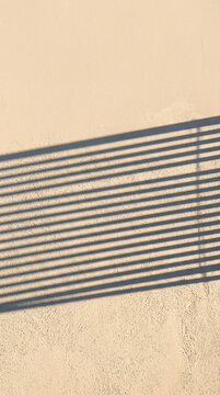 Minimalist architectural background featuring sharp parallel shadows cast by a railing onto a textured beige concrete wall creating a serene and modern aesthetic for design projects