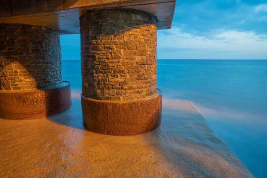 View of the stone pillars of the Fincantieri S.p.A. shipyard structure at the water's edge during twilight in Sestri Levante, Liguria, Italy.
