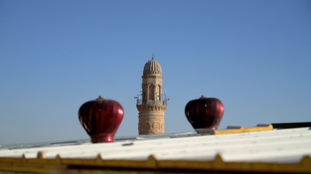 Ulu Cami minaret top, Great Mosque of Mardin, Turkey, seen between two red roof ventilators on a metal rooftop in the old town