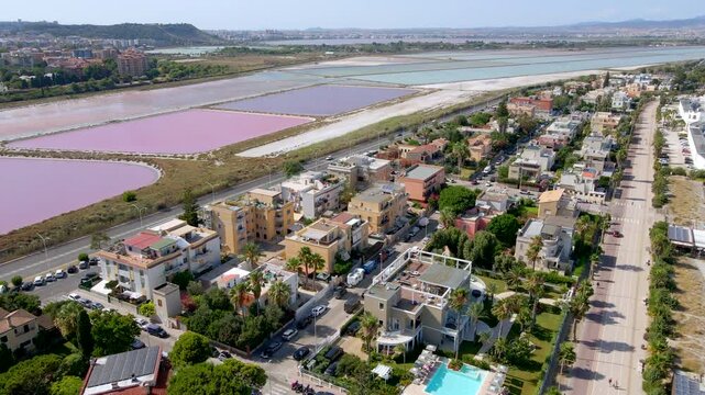 Aerial drone forward shot over colorful pink salt ponds of Cagliari, Sardinia, Italy, with Molentargius nature reserve and urban skyline