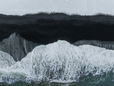 View of black sand beach with crashing white waves and foam on the shoreline in Iceland.