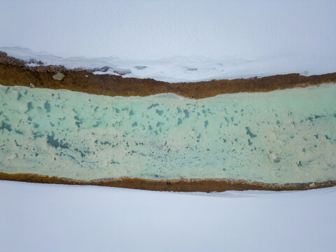View of a turquoise geothermal stream with mineral deposits and snow-covered banks, Iceland.