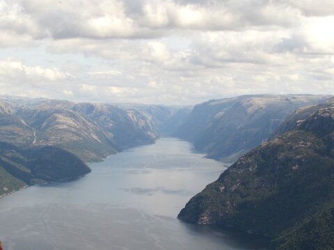 Breathtaking panoramic view looking down the length of a massive fjord, flanked by towering rocky mountains under a dramatic cloudy sky.