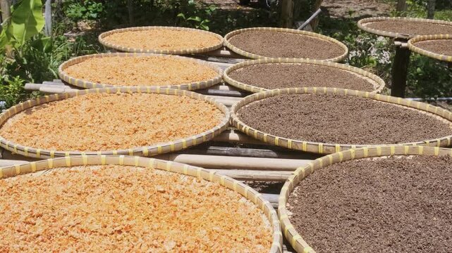 Round bamboo trays filled with black peppercorns and crushed red pepper dry under the sun in Phu Quoc island, Vietnam. Pepper cultivation and spice production. Traditional agricultural processing