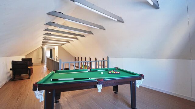 Attic billiard room with green table, cues, balls, slanted ceiling, linear lights, seating area, metal railing, minimalist design