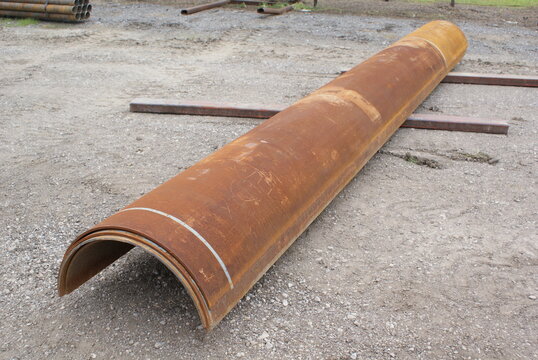 Rusty curved steel half pipe section lying on a gravel yard